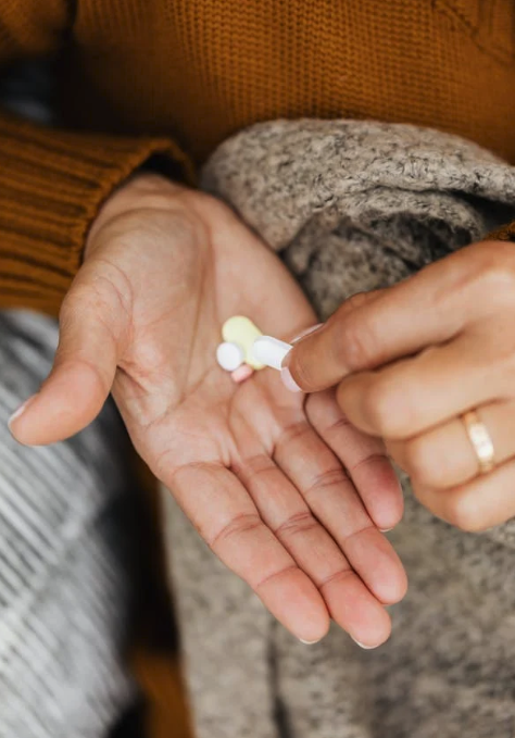 Hånd med piller Kvinde iført orange striktrøje holder en håndfuld piller